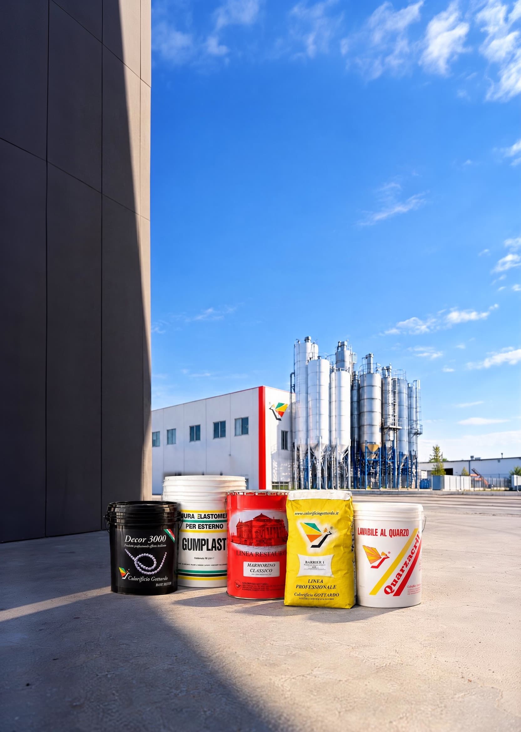 Secchi e sacchi di prodotti Colorificio Gottardo al sole sul piazzale dello stabilimento, con il capannone e i silos sullo sfondo