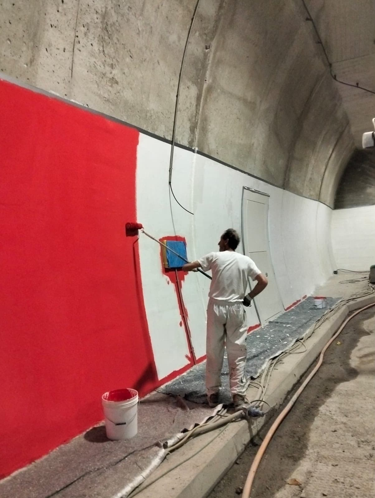 Applicatore che stende a rullo una pittura rossa sulla parete di una galleria