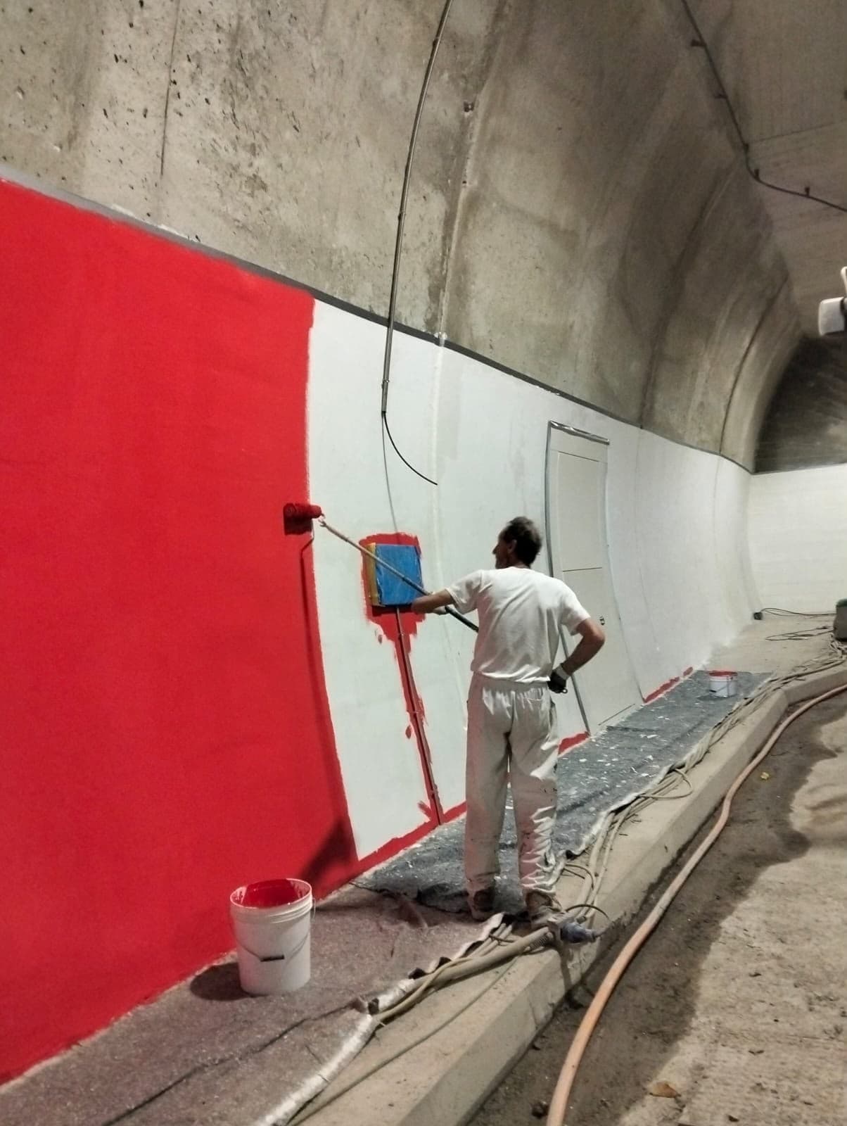 Applicatore che stende a rullo una pittura rossa sulla parete di una galleria
