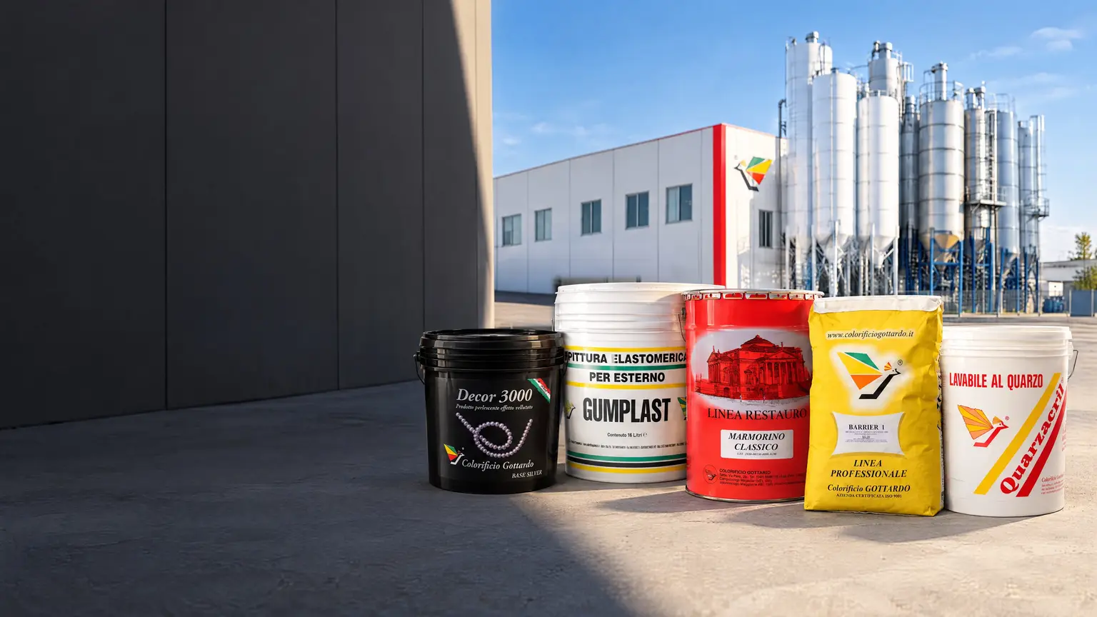 Secchi e sacchi di prodotti Colorificio Gottardo al sole sul piazzale dello stabilimento, con il capannone e i silos sullo sfondo